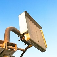 an internet network signal booster hanging on the roof by a rusty metal pipe with clear blue sky