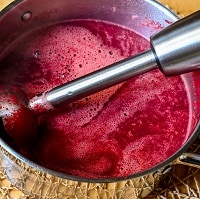 Immersion blender in pot with beetroot soup.