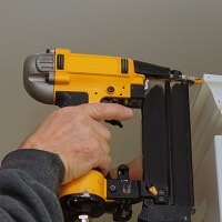 Carpenter brad using nail gun to Crown Moulding on kitchen cabinets